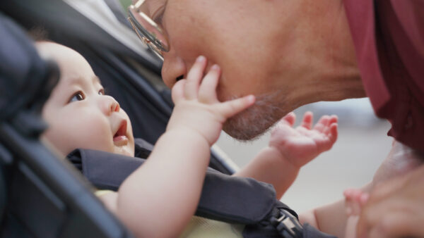 Baby in car seat looks at father and touches father's face.